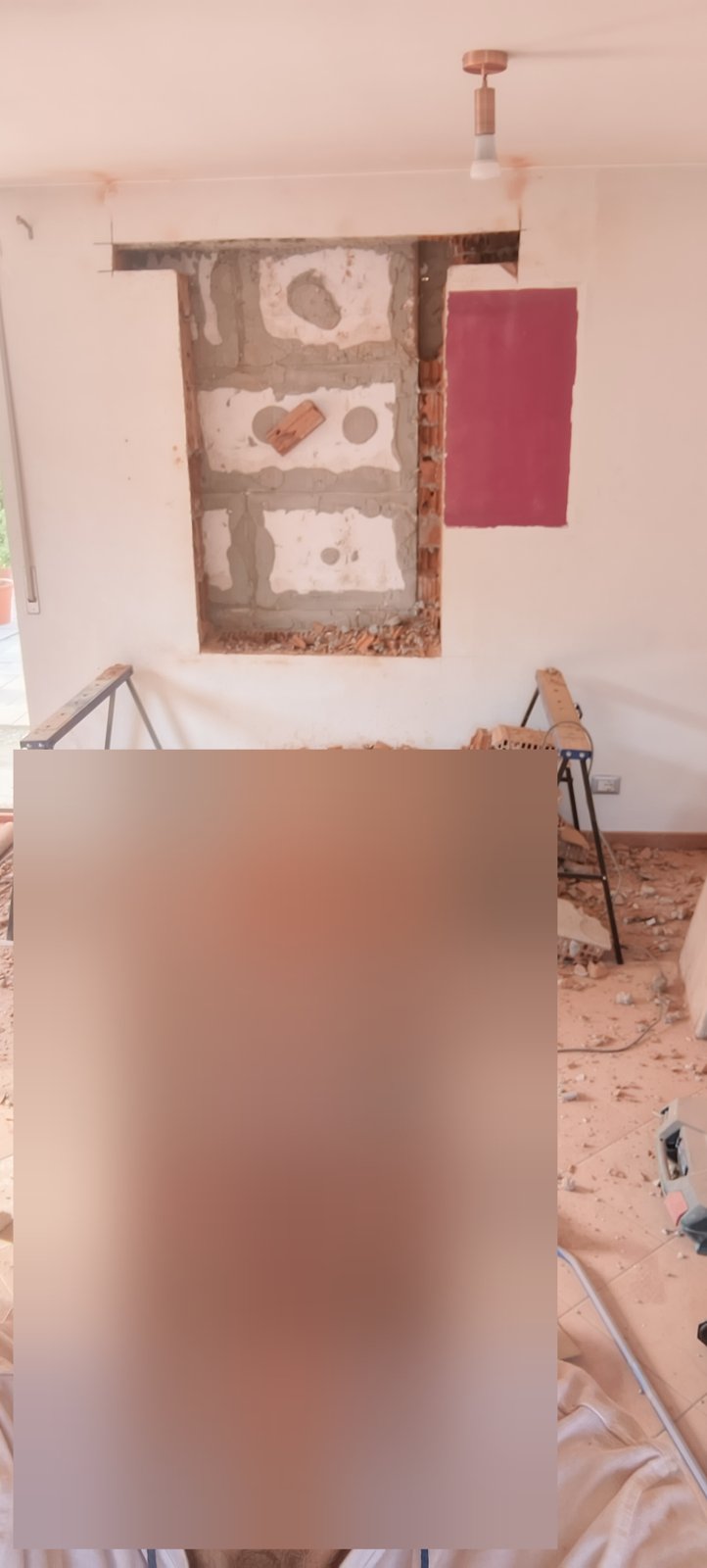 Apertura nella parete con blocchi e malta a vista, macerie a terra e due cavalletti da lavoro
